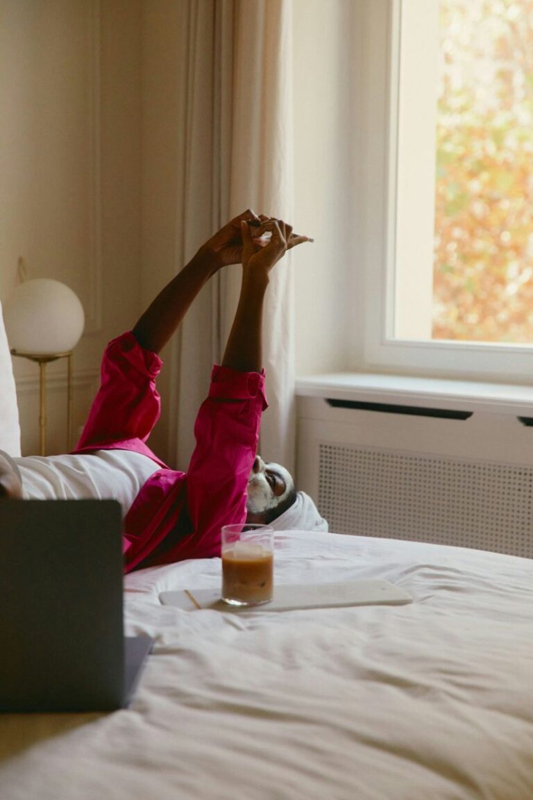 woman with face mask lying on bed looking at phone